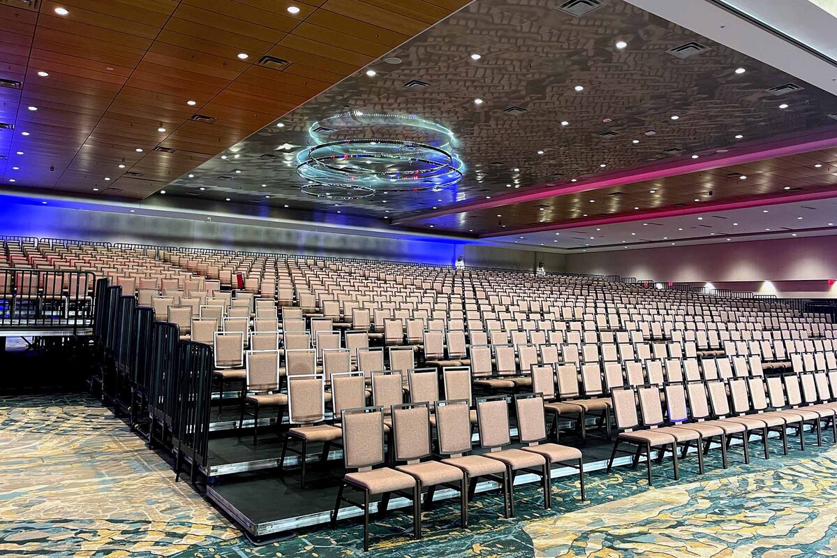 Tiered audience risers filled with rows of chairs in a hotel ballroom, facing the stage