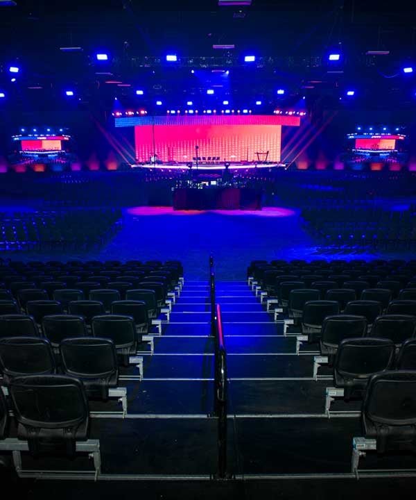 Arena concert stage with LED wall and lighting rig, seen from tiered audience seating