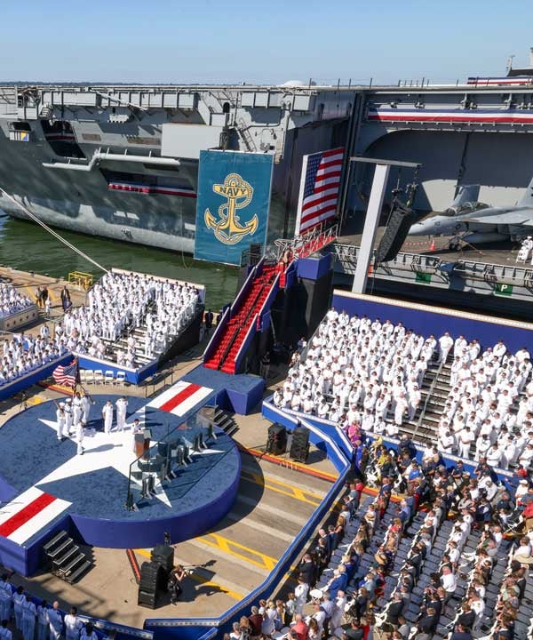 Navy ceremony stage and grandstands on a pier beside an aircraft carrier