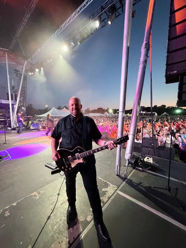 Performer with guitar on an outdoor PM1 stage at dusk for a Gary Sinise Foundation concert