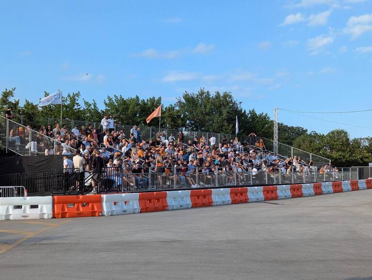 Crowd seated in PM1 temporary stadium seating with flags along the front rail