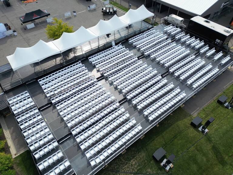 Rows of white chairs on a PM1 tiered platform outdoors, with tents around it