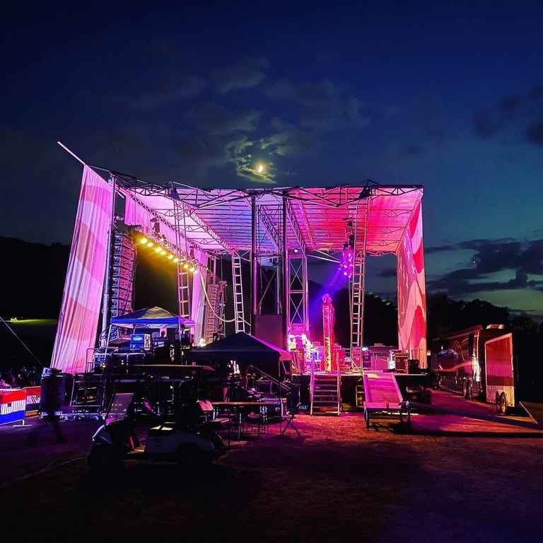 Outdoor PM1 stage lit pink and purple with scaffold towers and a canopy