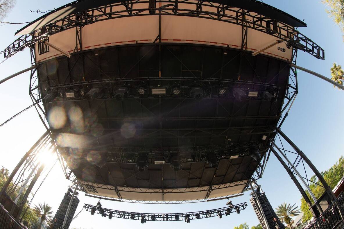 Round PM1 stage with a black truss roof and lighting rig set up outdoors among palm trees