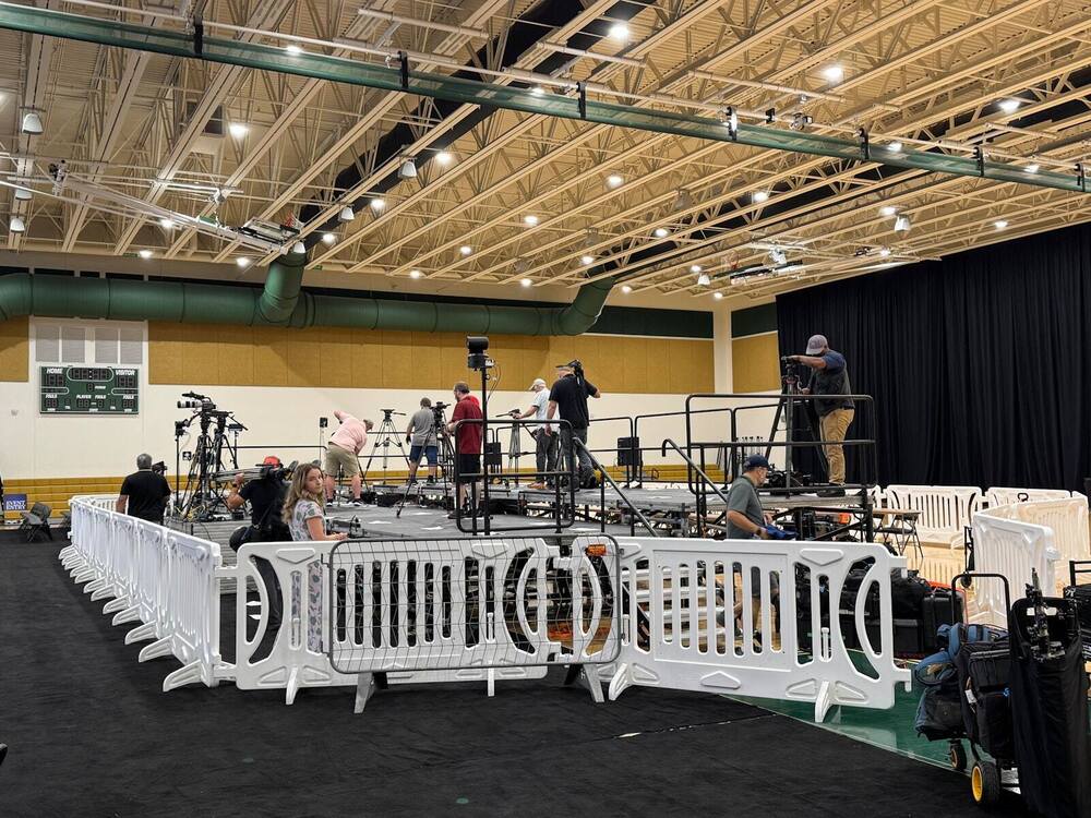 Press and camera risers behind barricade inside an arena, set for a political event
