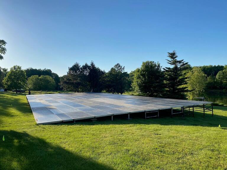 Large PM1 modular platform on a scaffold base, leveled on uneven ground beside a lake