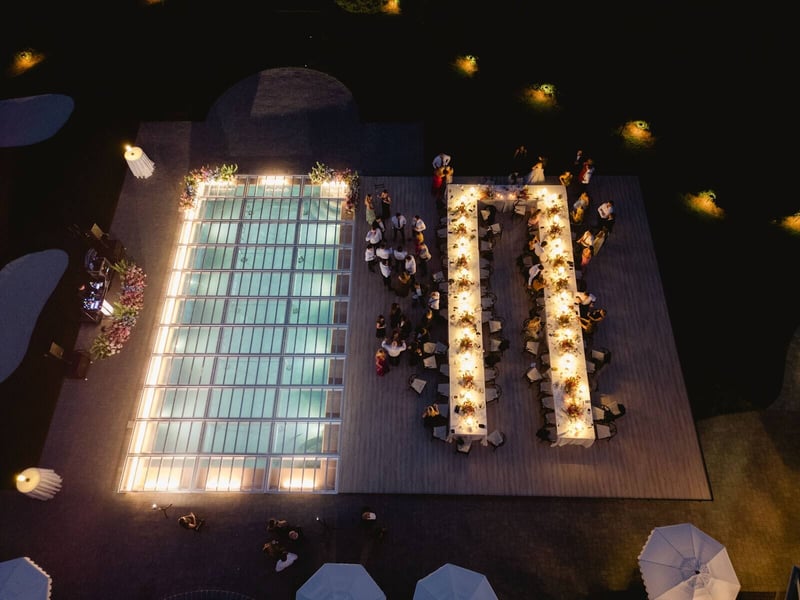 Aerial view at night of an illuminated pool and dining tables at a Detroit-area estate event