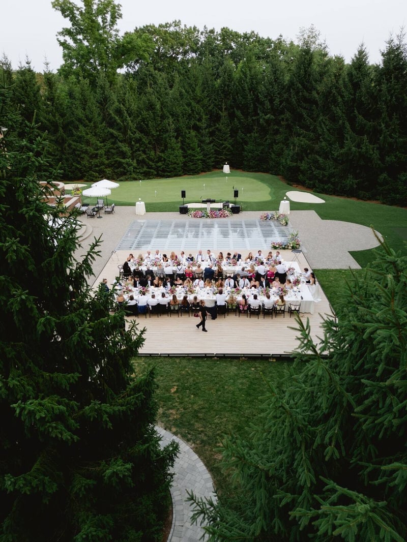 Guests seated at long tables under a clear roof on the lawn at a Detroit-area estate event