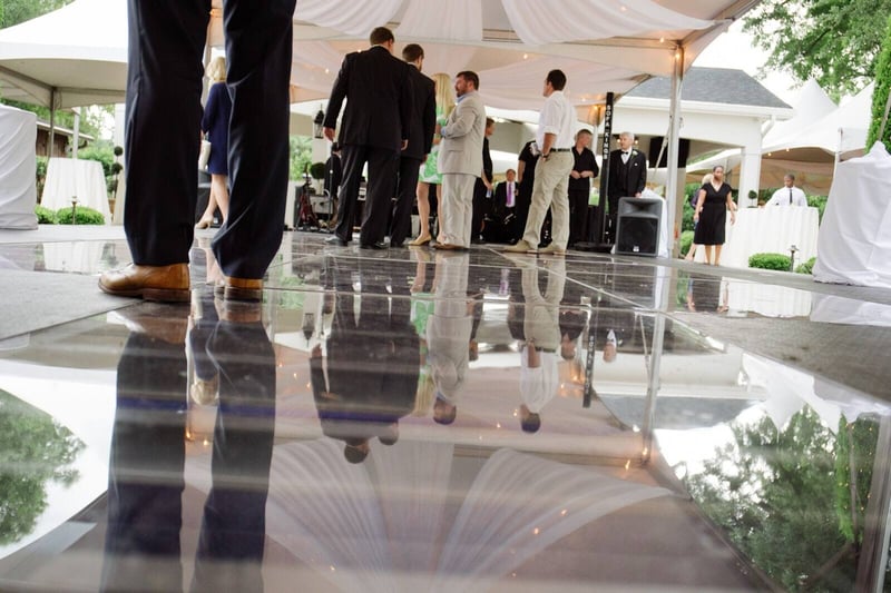 Guests in formal wear on a reflective pool cover floor under a white event tent