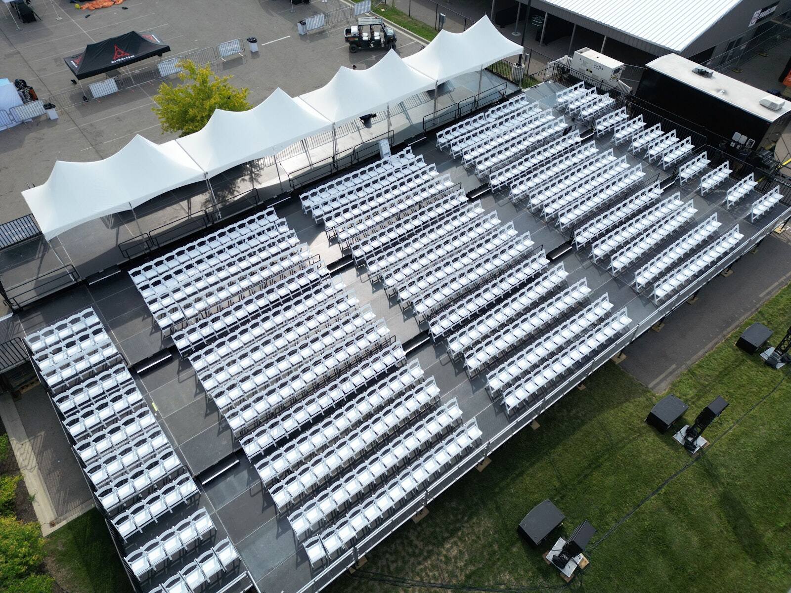 Rows of white chairs on a PM1 tiered platform outdoors, with tents around it