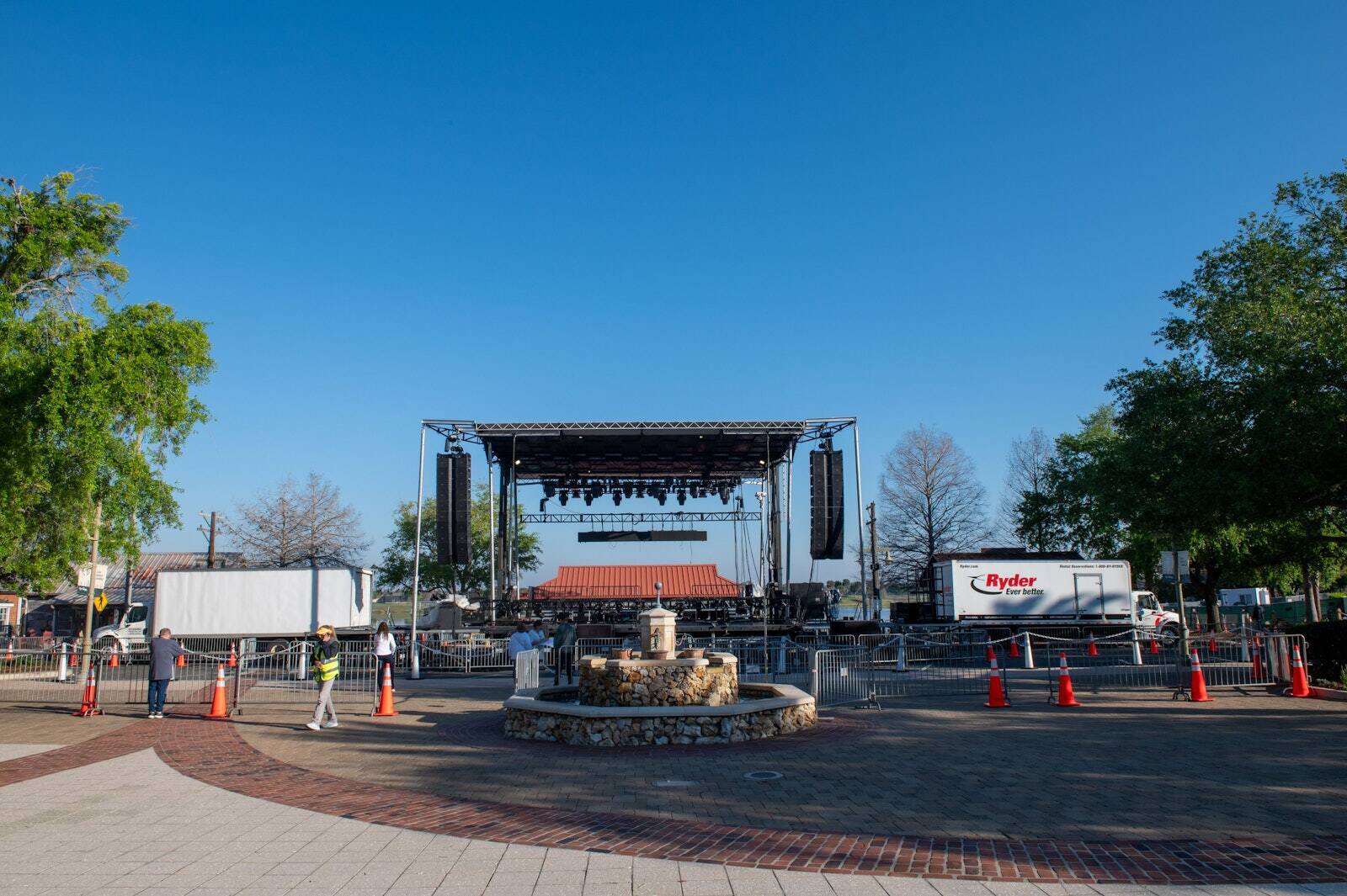 PM1 outdoor stage with a red roof and side speakers on a plaza behind a stone fountain