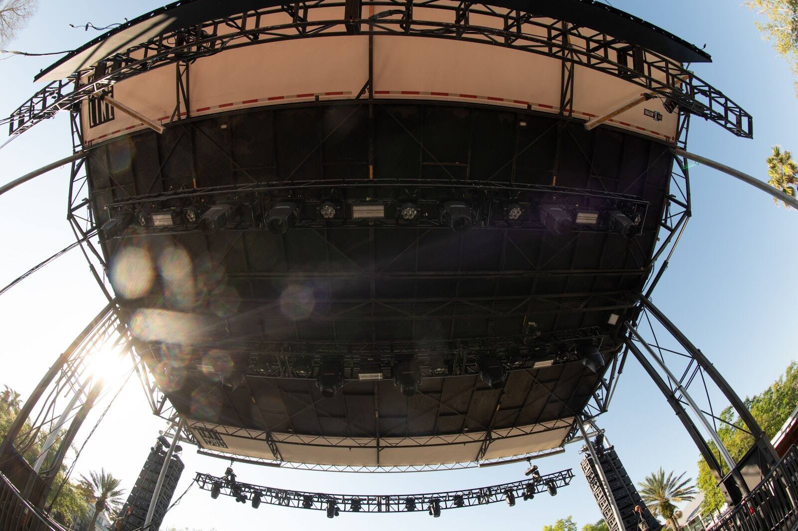 Round PM1 stage with a black truss roof and lighting rig set up outdoors among palm trees
